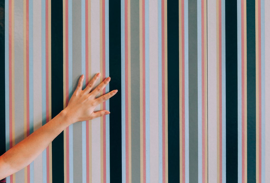 a hand touching striped peel and stick wallpaper