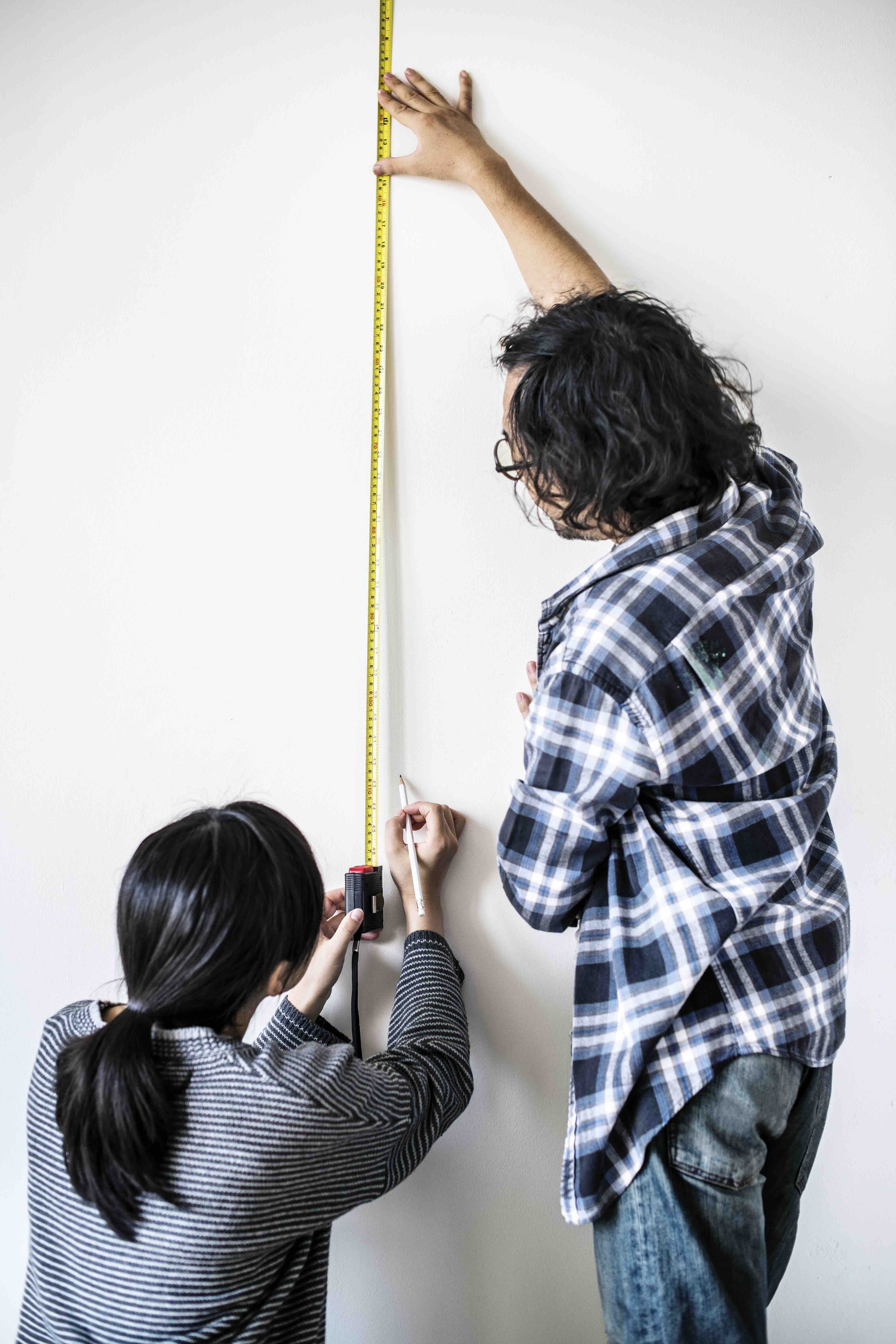 Couple measuring a wall with a tape measure, planning a home improvement project together.