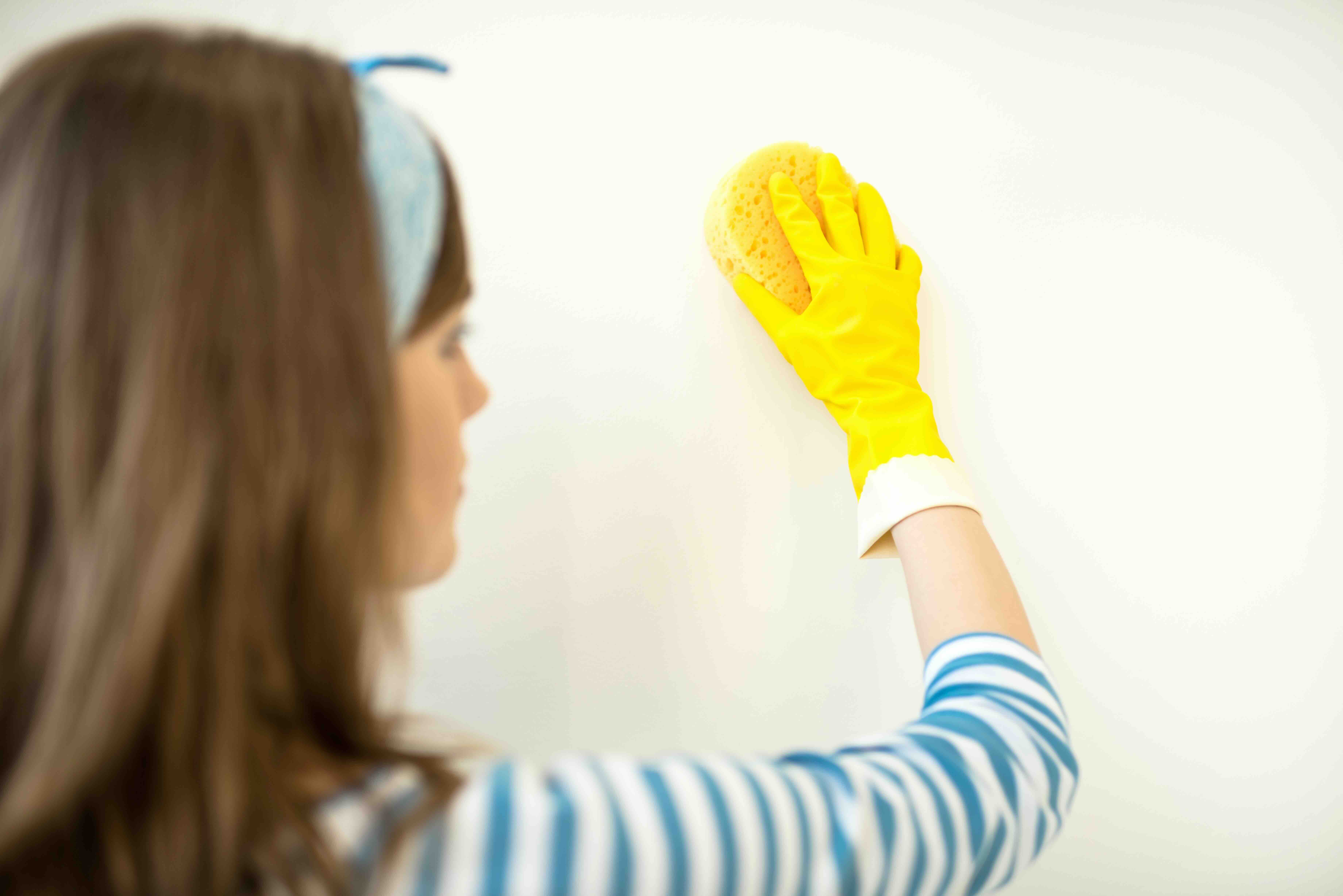 Woman cleaning apartment wall with alcohol to prepare for wallpaper installation, ensuring a smooth surface for adhesion.
