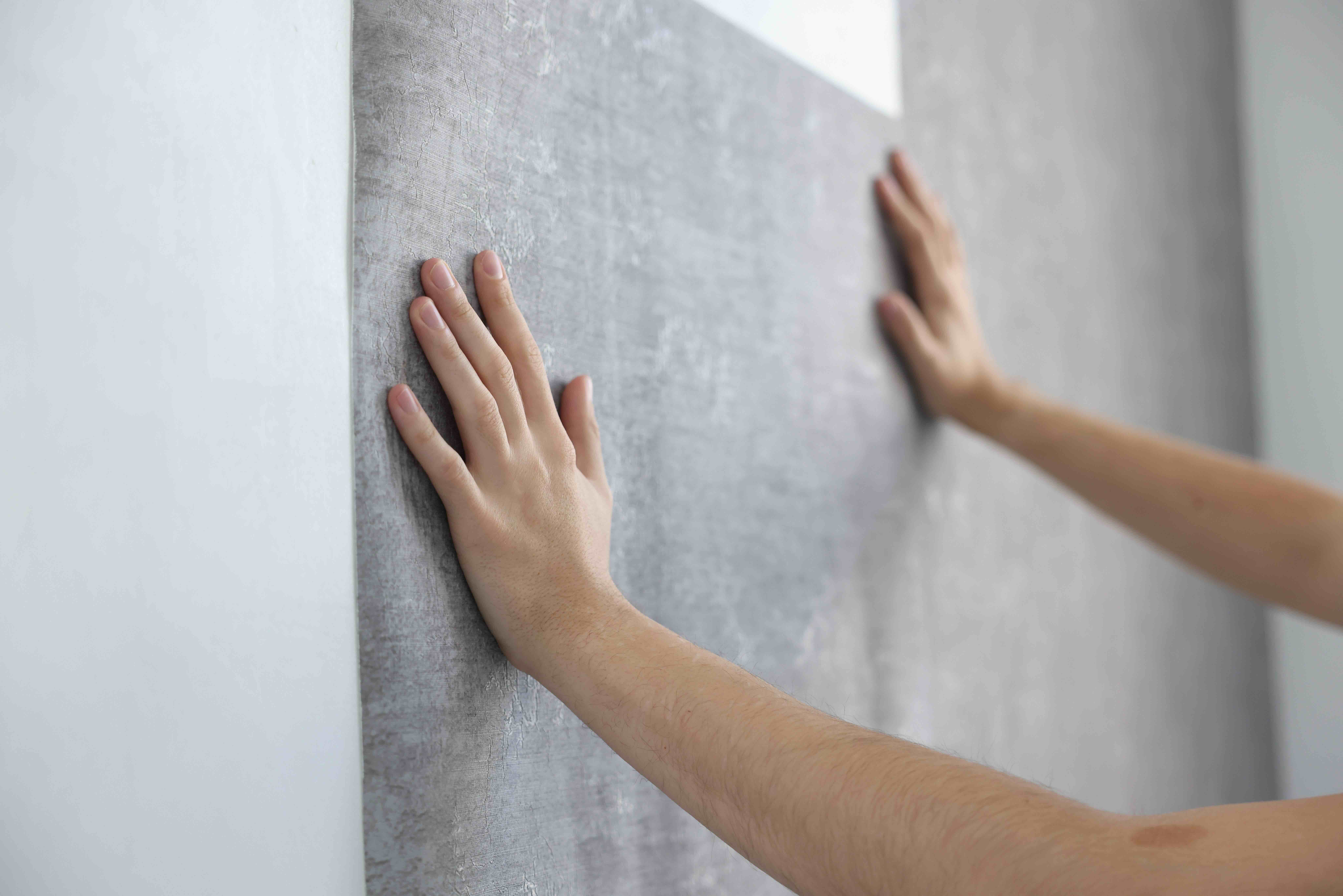 Renter aligning seams while applying renter-friendly wallpaper in a stylish living room.