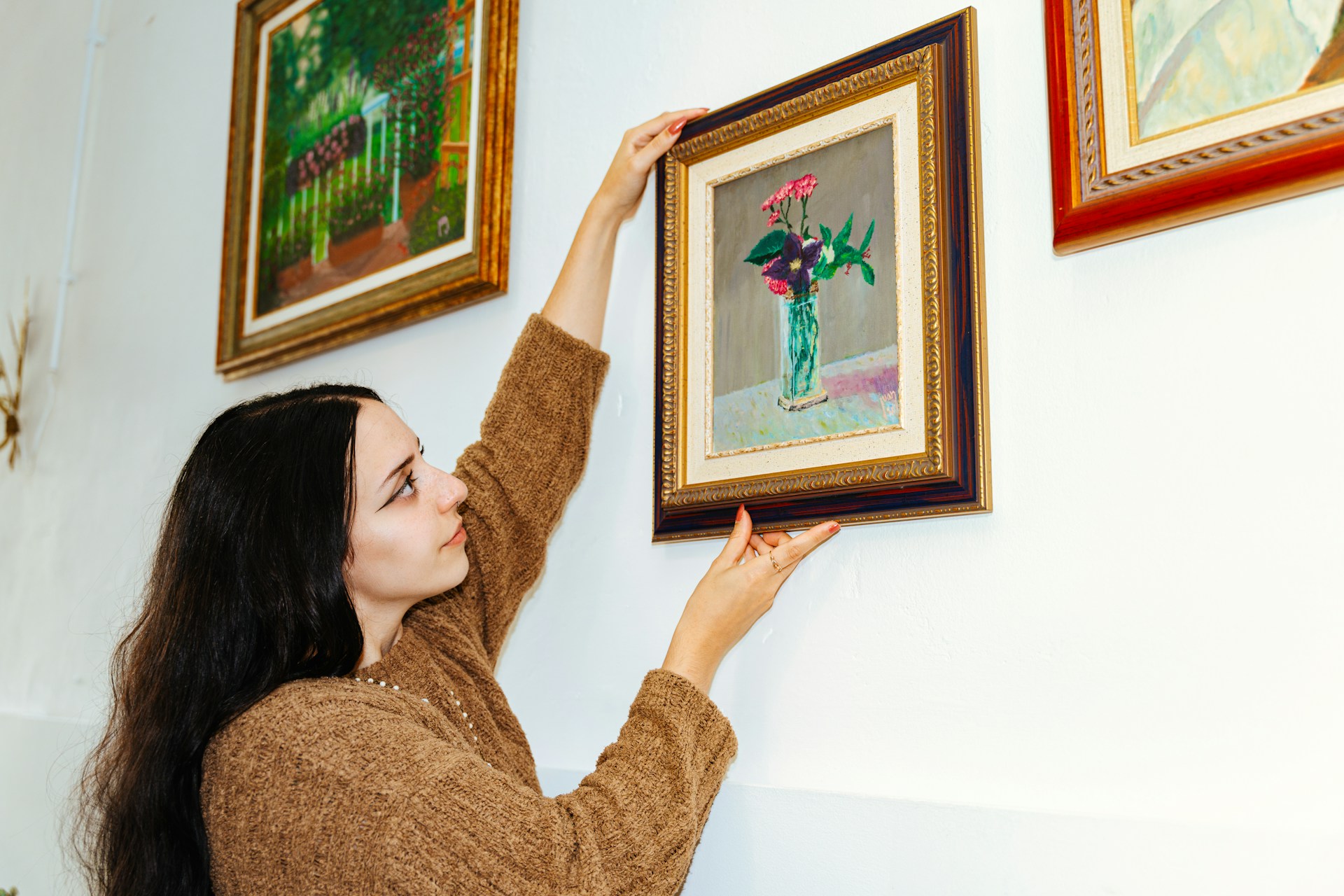 Renter hanging framed artwork on her apartment wall using 3M Command strips for a stylish and damage-free decoration.